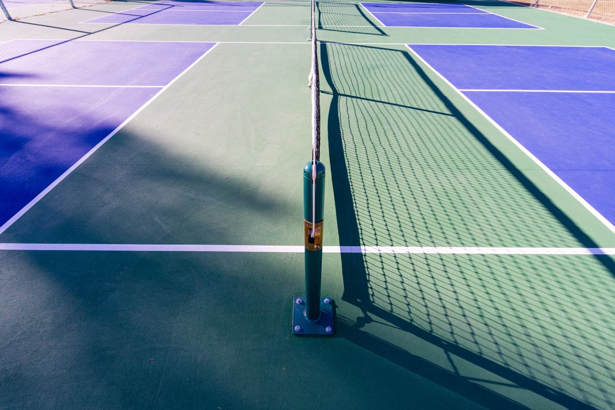 A net and white court lines on an empty blue and green pickleball court.