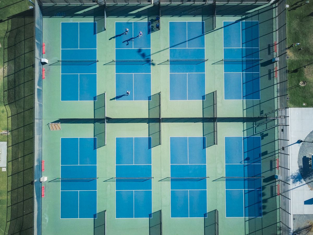 A view from above of blue tennis courts and green surrounds.