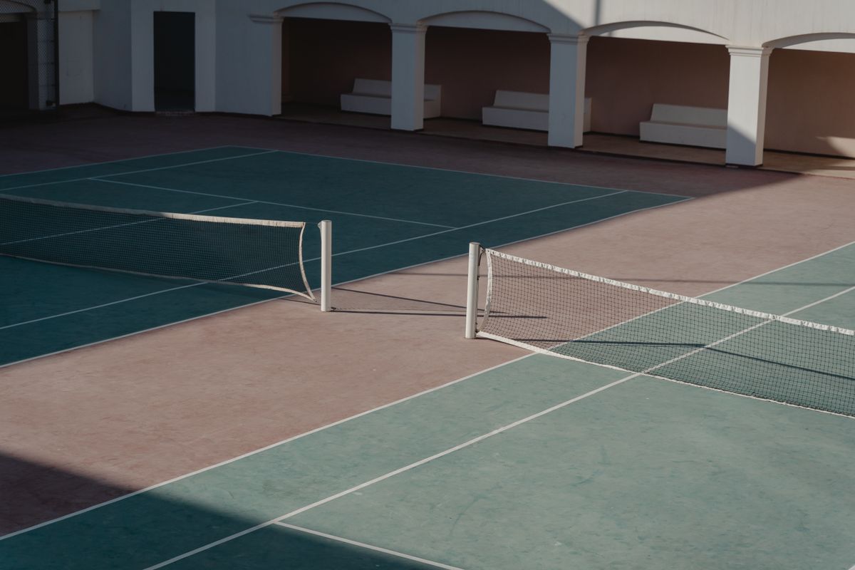 A quiet blue tennis court, with white benches and afternoon shadows.